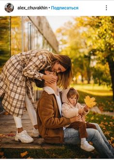 a woman holding a baby while sitting next to another woman on the ground with leaves in front of her