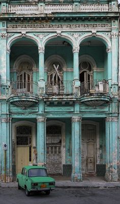 an old green car parked in front of a blue building with columns and balconies