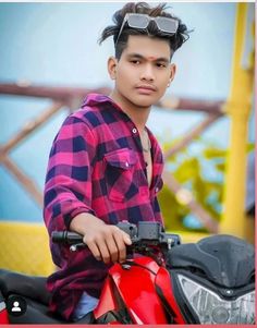 a young man sitting on top of a red motorbike with sunglasses on his head