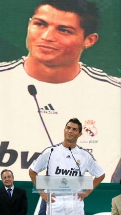 a man standing at a podium in front of a large poster with a soccer player on it