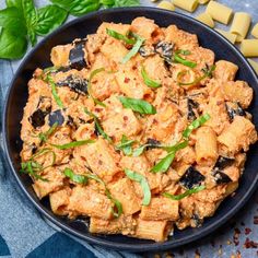 a black bowl filled with pasta and meat on top of a blue table cloth next to green leaves