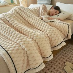 a woman laying on top of a bed covered in a blanket next to a pillow