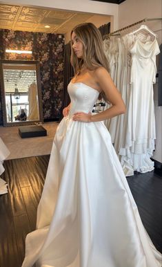 a woman in a white wedding dress standing next to a rack of dresses on display