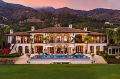 a large white house with a pool in the front yard and mountains in the background