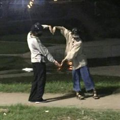 two people holding hands while standing on a sidewalk at night with fireworks in the background