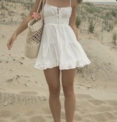 a woman standing on top of a sandy beach holding a straw bag and wearing sandals