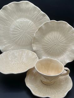 three white dishes and two cups on a black tablecloth with an image of a flower in the center