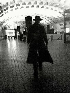 black and white photograph of a man walking through a subway station with an umbrella over his head