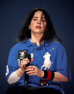 a woman in a blue polo shirt holding a microphone and looking up at the sky