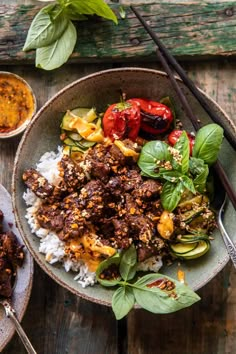 a bowl filled with meat and vegetables on top of rice next to chopsticks