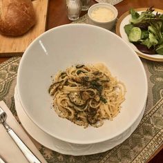 a white bowl filled with pasta on top of a table next to bread and salad