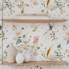 two shelves with vases and books on them against a floral wallpapered background