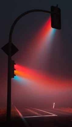 an empty street at night with traffic lights shining on the road and fog in the air