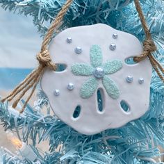 a white sand dollar ornament hanging from a blue christmas tree