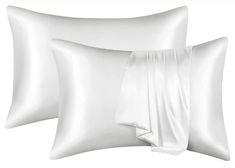 two white pillows with satin sheets on them