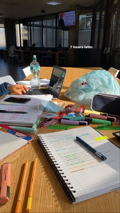 two people sitting at a table with notebooks and papers on it, one person is using a laptop