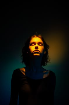 a woman with her eyes closed standing in front of a black background and yellow light