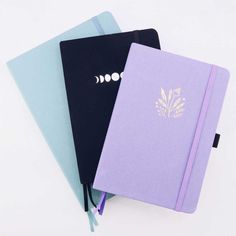 three different colored notebooks sitting next to each other on top of a white surface