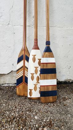 three wooden paddles sitting next to each other on top of the ground in front of a white wall