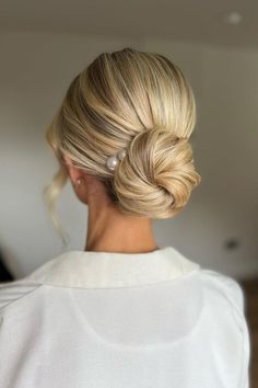 a woman with blonde hair styled into a low bun, wearing a white sweater and pearl earrings