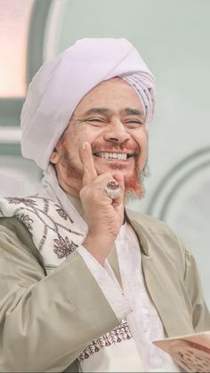 a man in a turban smiles as he holds his finger to his mouth