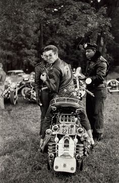 black and white photograph of two men standing next to a motorcycle with an engine on it