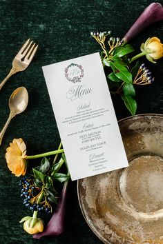 a menu sitting on top of a metal plate next to flowers and silver utensils