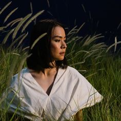 a woman sitting in tall grass with her head turned to the side and eyes closed