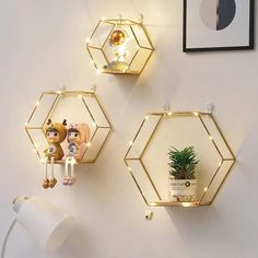 three gold hexagonal shelves with lights on the wall above them and a potted plant next to it