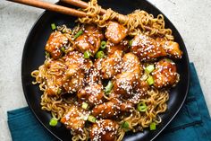 a black plate topped with meat and noodles next to chopsticks on a blue napkin