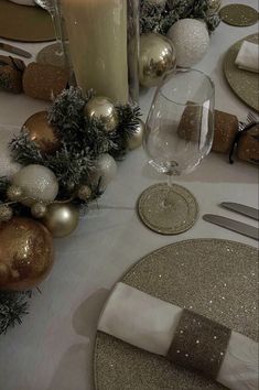 the table is set for christmas dinner with silver and gold decorations, candles, and plates