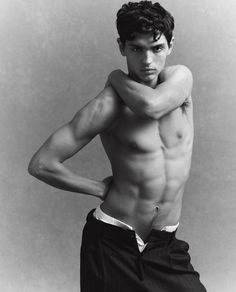 a shirtless young man posing for a black and white photo with his hands on his hips