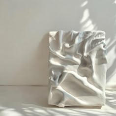 a white sculpture sitting on top of a floor next to a wall with shadow coming from it