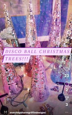 there are many disco ball christmas trees in the room and one is pink with white letters