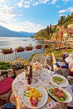 an outdoor dining area overlooking the water and mountains with flowers in bloom on the table