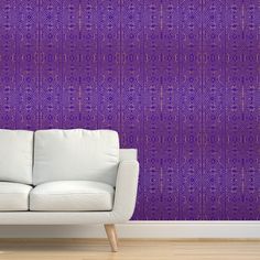 a white couch sitting in front of a purple wall with an intricate pattern on it