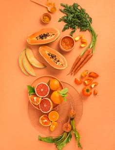 an assortment of fruits and vegetables are arranged on a pink surface with oranges, carrots, lemons, and parsley