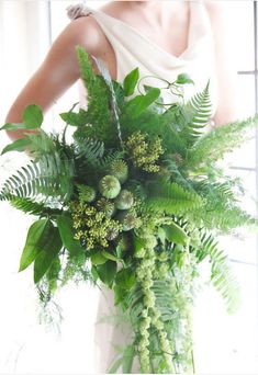 a woman in a white dress holding a large bouquet of green plants and foliages