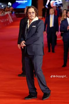 a man in a suit and tie standing on a red carpet with other people behind him