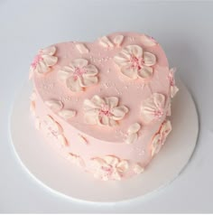 a heart shaped cake with pink frosting and flowers on it's side sitting on a white plate