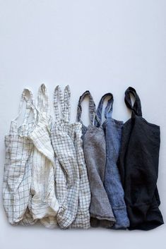 four different colored linen bags are lined up on the floor, one is black, one is white and one is gray