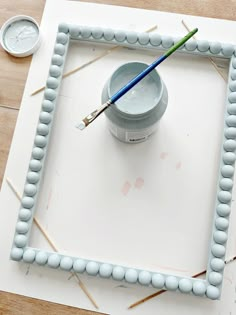 a paintbrush sitting on top of a white square with bead border around it