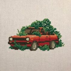 a cross stitch picture of an old red truck driving down the road with trees on it