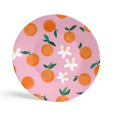 a pink plate with oranges and daisies on the rim, against a white background