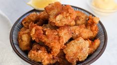 a bowl filled with fried food next to a lemon wedge on top of a table