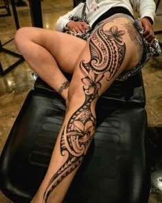 a woman sitting on top of a chair with a tattoo on her leg