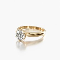 a yellow gold engagement ring with a single diamond in the center, on a white background