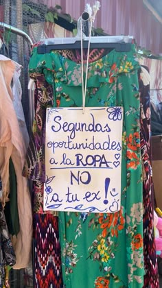 a sign is hanging on a clothes rack in front of other clothing and apparel items