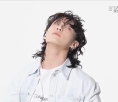 a man with curly hair looking up into the sky while wearing a white shirt and jeans