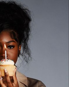 a woman holding a cupcake with a lit candle in her mouth